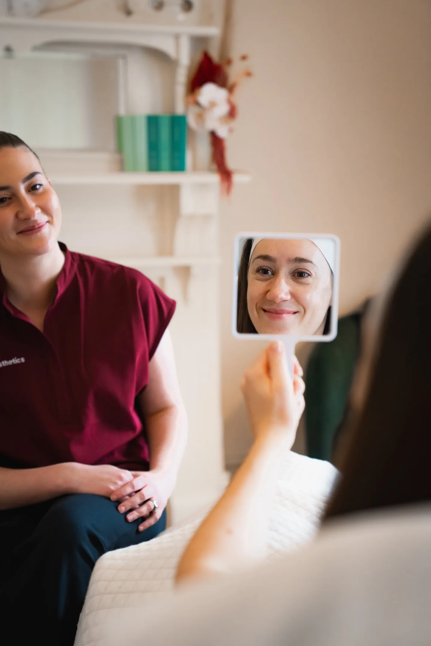 A client smiles into a hand mirror while a clinician looks on in the warm Embrace lounge