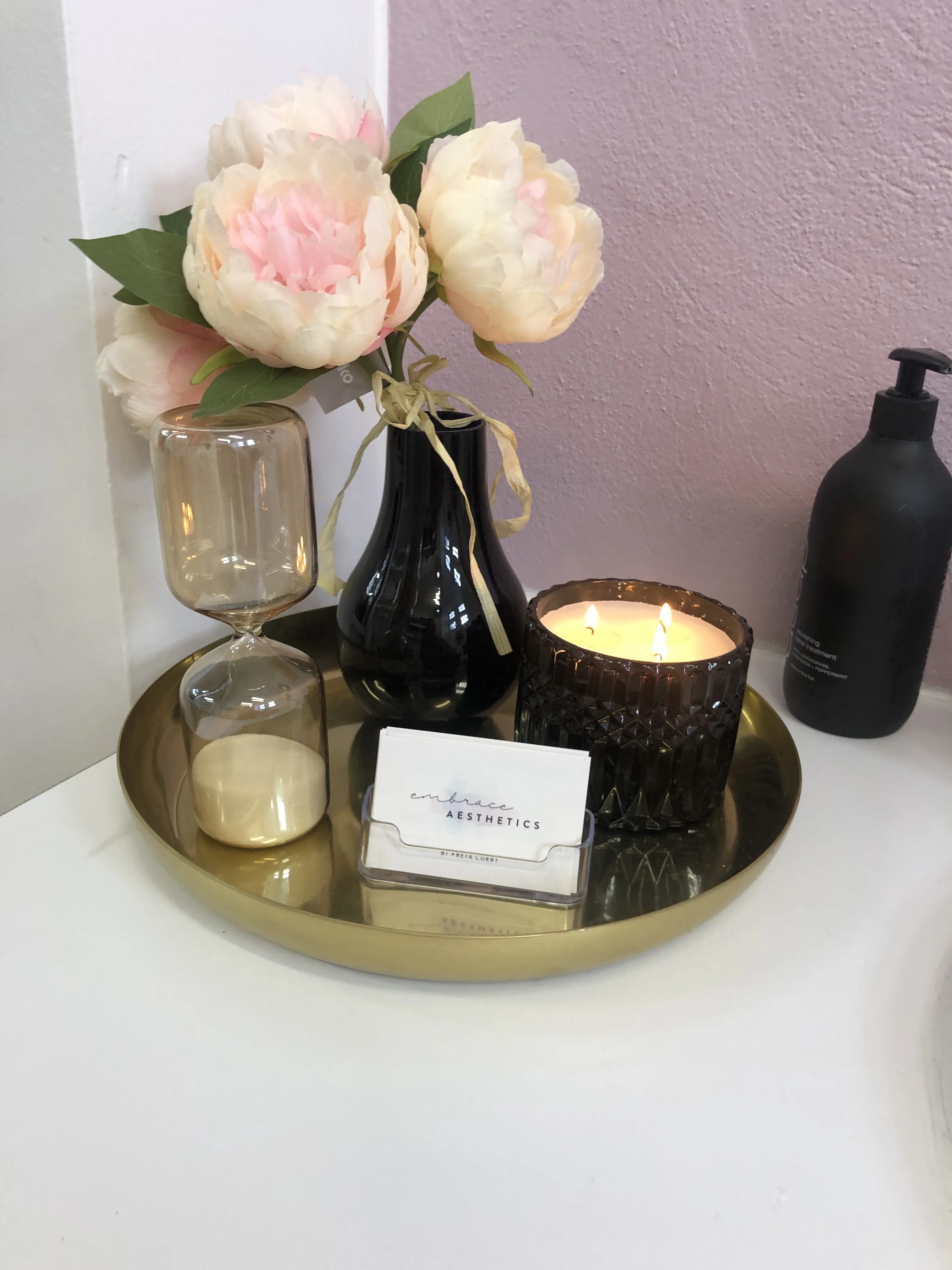 A gold styling tray with the Embrace Aesthetics card — the clinic's signature ambient detail