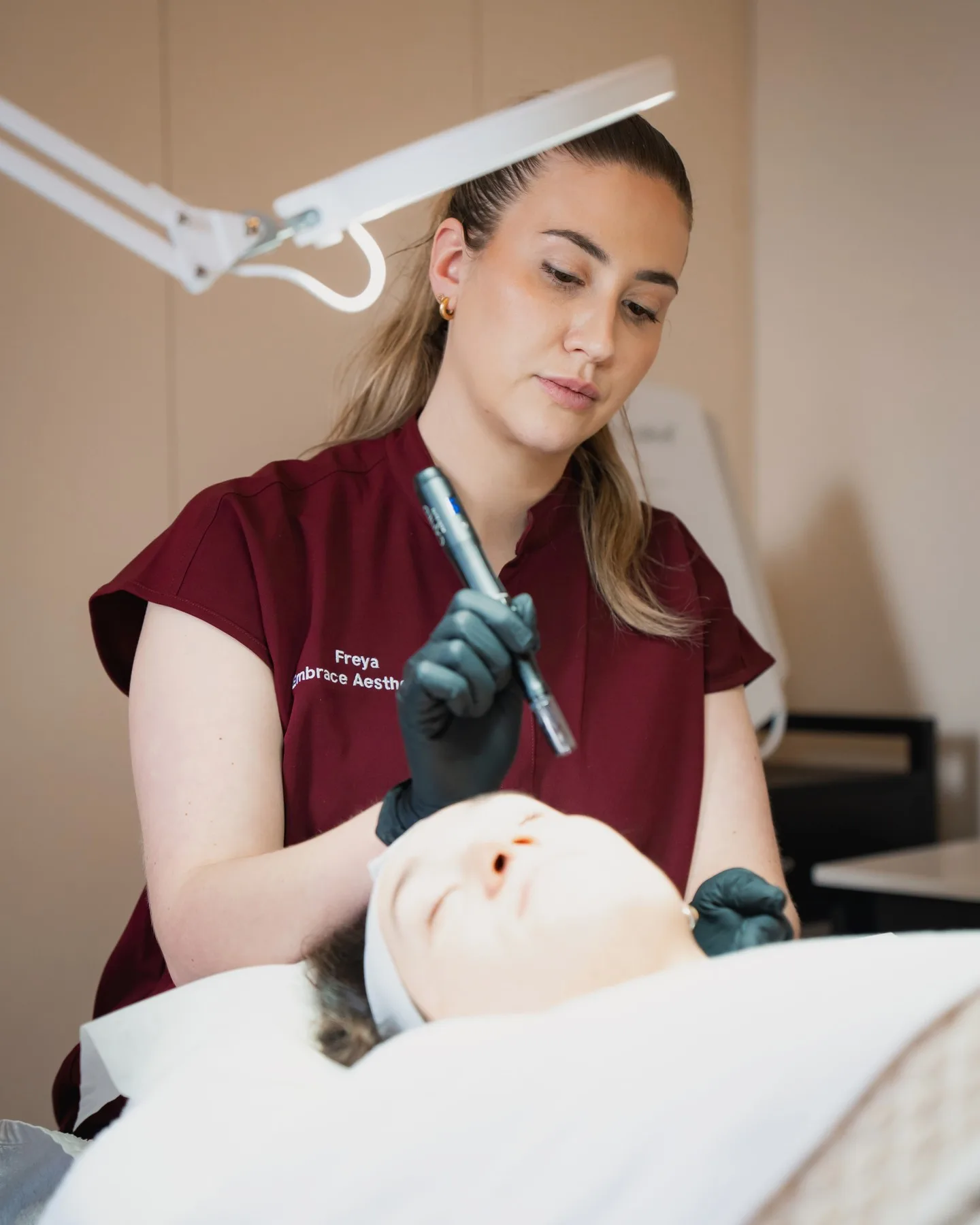 Freya guiding a skin-treatment pen over a client's face under a warm magnifying lamp at the Embrace clinic
